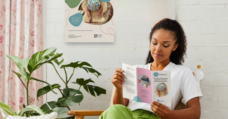 Mockup-Foto einer Person, die einen aufgeklappten Flyer des Stoffwindelverein e.V. liest. Im Hintergrund hängt ein passendes Poster an der Wand. Beide Materialien zeigen das Corporate Design des Vereins mit Stoffwindel-Motiven